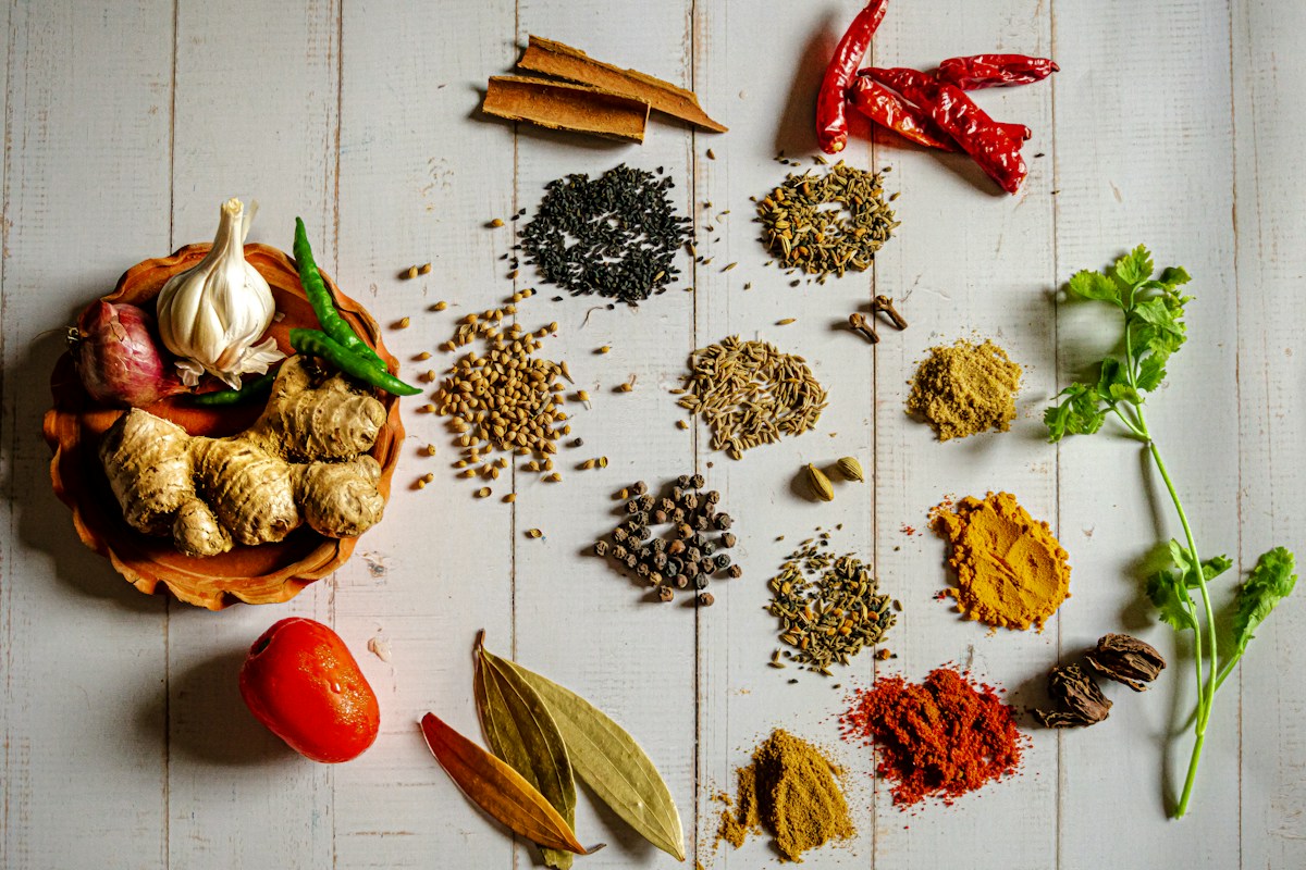 A glass spice jar filled with vibrant homemade taco seasoning powder surrounded by whole cumin seeds, smoked paprika, and chili flakes