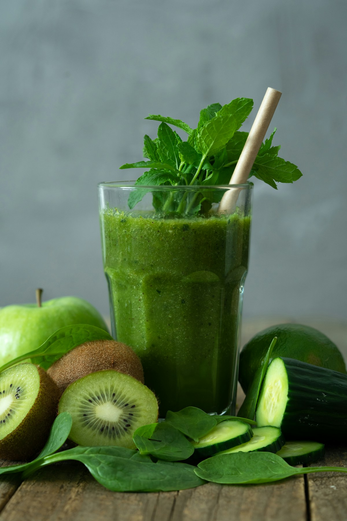 Vibrant emerald green detox smoothie in a glass with straw garnished with fresh mint, cucumber, and green apple