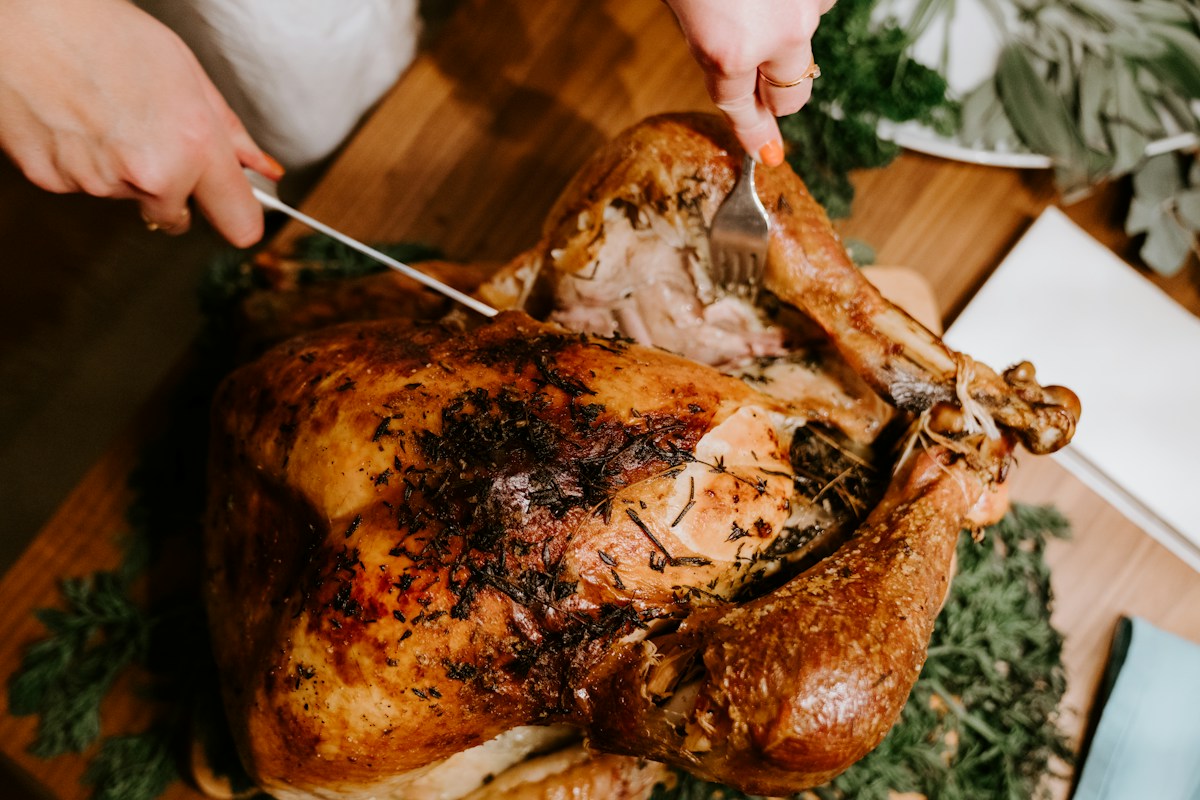 A whole golden roasted Thanksgiving turkey on a carving platter garnished with fresh rosemary, oranges, and cranberries